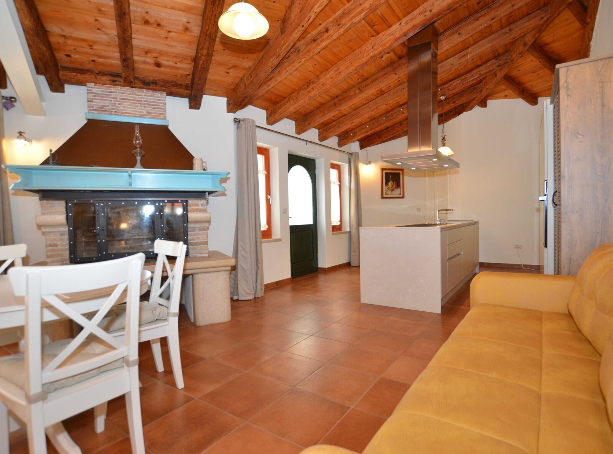 A cozy interior with a wooden ceiling, a kitchen area with a blue countertop, a dining table with chairs, and a yellow sofa.