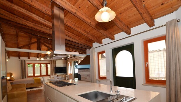 Una cocina amplia con una isla central, vigas de madera en el techo y ventanas grandes.
