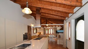 Una cocina moderna con una isla central, vigas de madera en el techo y una zona de comedor con mesa y sillas.