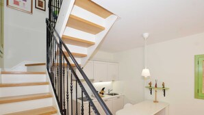 Un escalier avec des marches en bois et des balustrades noires mène à un espace cuisine doté de meubles blancs et d'une table à manger avec des chaises.