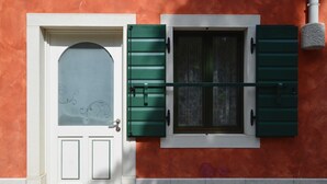 Une porte blanche avec un panneau de verre et des volets verts, placée devant un mur rouge avec un plinthe blanche et une petite fenêtre également dotée de volets verts.