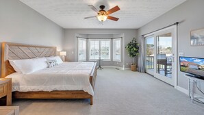 Ein Schlafzimmer mit einem großen Bett, einem Deckenventilator, einem Fernseher und Blick ins Freie.
