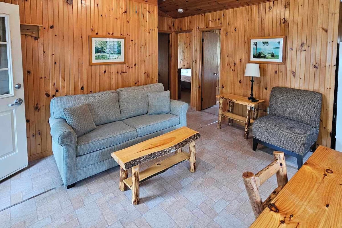 A wooden-paneled room with a sofa, a wooden coffee table, a chair, and a ceiling fan.