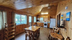 Une cuisine aménagée dans le style d’un chalet, avec des murs en bois, une table à manger, des chaises, un poêle, un réfrigérateur et un téléviseur.