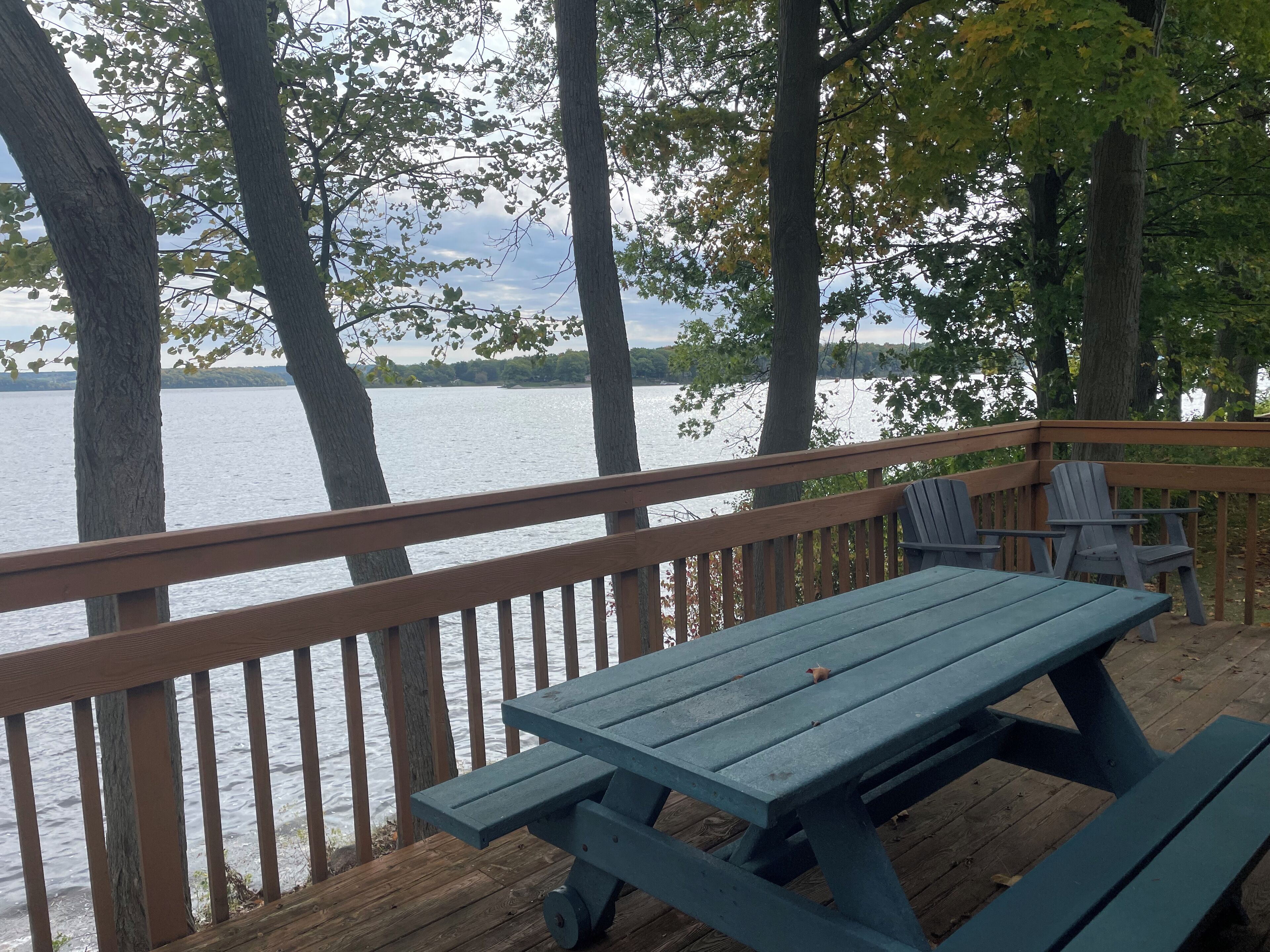 Une terrasse en bois avec une table de pique-nique et des chaises, donnant sur une étendue d’eau.