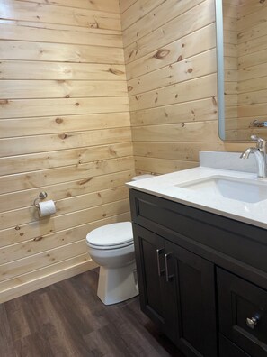 A bathroom with wooden panel walls, a white toilet, a dark-colored vanity with a mirror, and a white sink. - Southview Cottages Resort (Bailieboro)