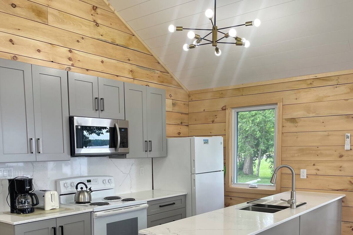 A modern kitchen with grey cabinets, a stainless steel refrigerator, a stove, and a coffee maker.