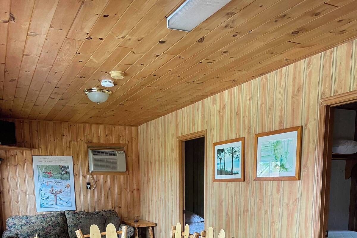 A wooden cabin interior with a dining table and chairs, a sofa, and two framed pictures on the walls.