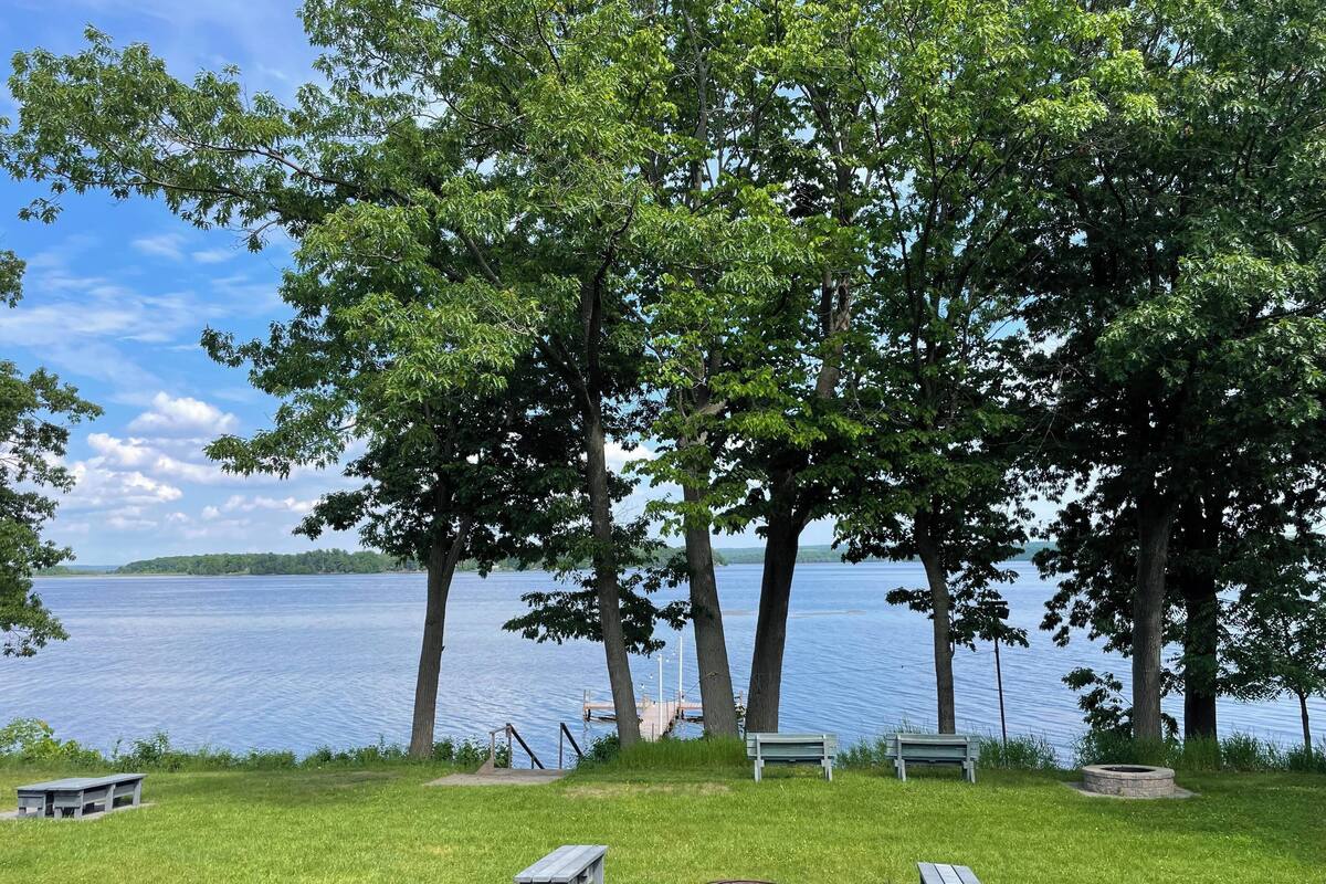 A lakeside park with picnic tables and benches, surrounded by trees and a view of the water.