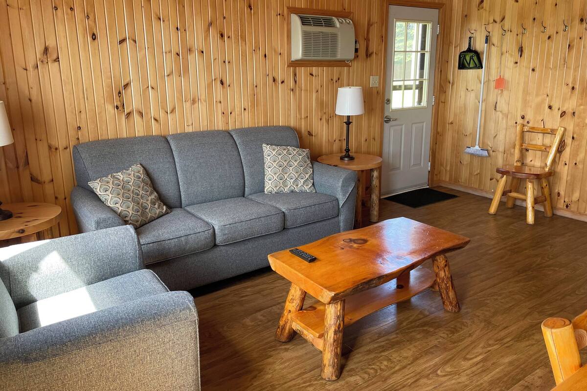 A cozy room with a grey sofa, a wooden coffee table, a wooden chair, a lamp, and a door with a window.