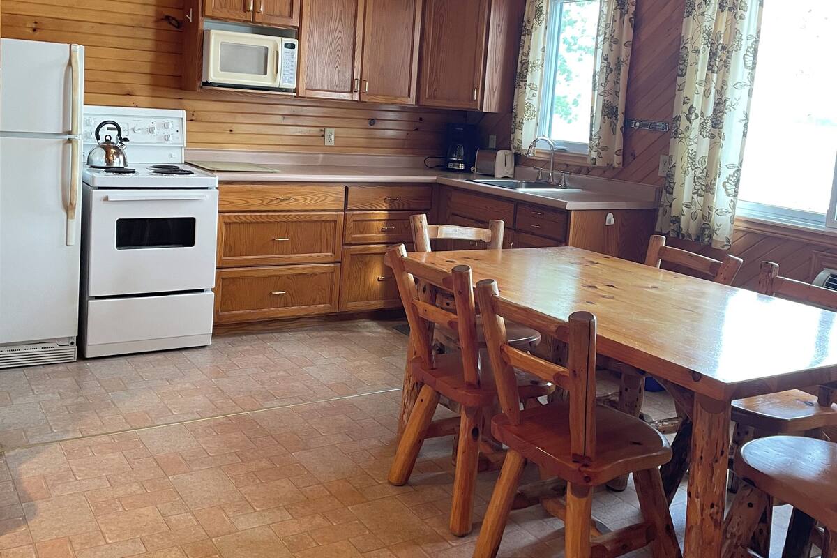 A wooden cabin kitchen with a stove, microwave, and wooden cabinets.