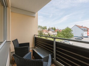 A balcony with wicker furniture, a view of a street with parked cars, and buildings in the background.