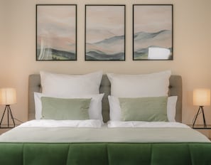 A hotel room with a bed, two bedside lamps, and three framed landscape paintings on the wall.