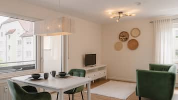 Ein modernes Wohnzimmer mit einem weißen Tisch, grünen Stühlen, einem Flachbildfernseher und einer Deckenleuchte.