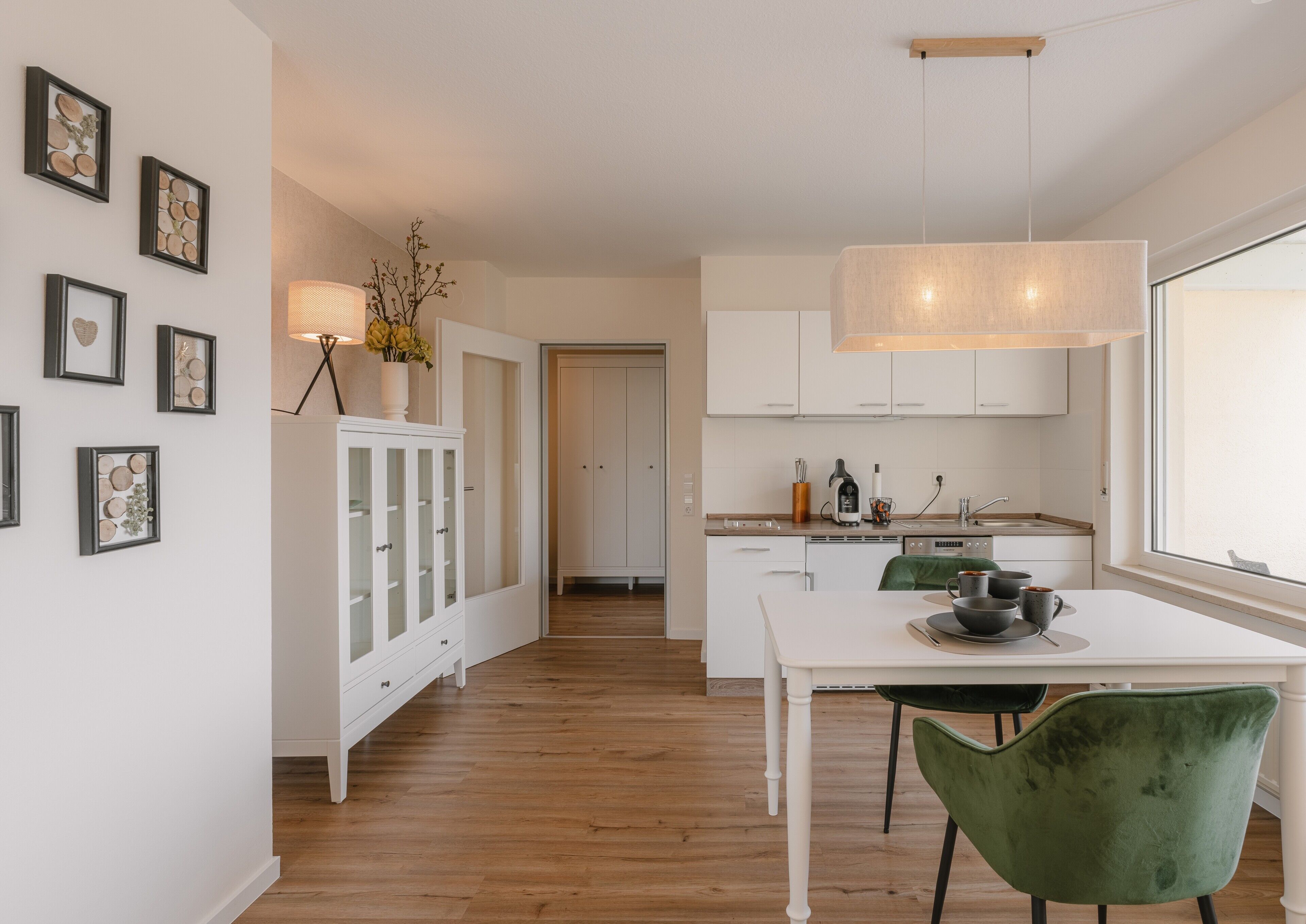 A modern kitchen with white cabinetry, a dining table with chairs, and a large window.