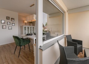 A modern living room with a dining area, a green chair, and a view through a large window.