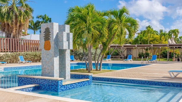 Piscina com azulejos de mosaico azul, rodeada por palmeiras e cadeiras de descanso.