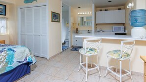 Ein Zimmer mit Bett, Schreibtisch mit zwei Stühlen, Küchenzeile, Badezimmer und Wasserspender.