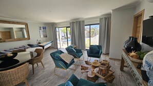 A spacious living area with a pool view, wicker furniture, teal sofas, and a wooden coffee table.