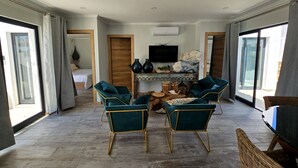 A spacious living area with a large TV, two green velvet armchairs, and a wooden coffee table.