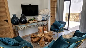 A modern living room with teal upholstered chairs, a wooden coffee table, and a flat-screen TV mounted on the wall.
