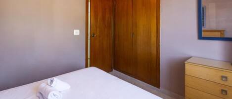 Una habitación de hotel con una cama, un armario de madera, un tocador y un espejo en la pared.