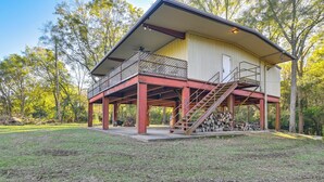 A two-story building with a balcony and a staircase leading to a covered area with a stack of firewood. - Riverfront Fishing: Home in Columbus w/ Grill (Columbus)