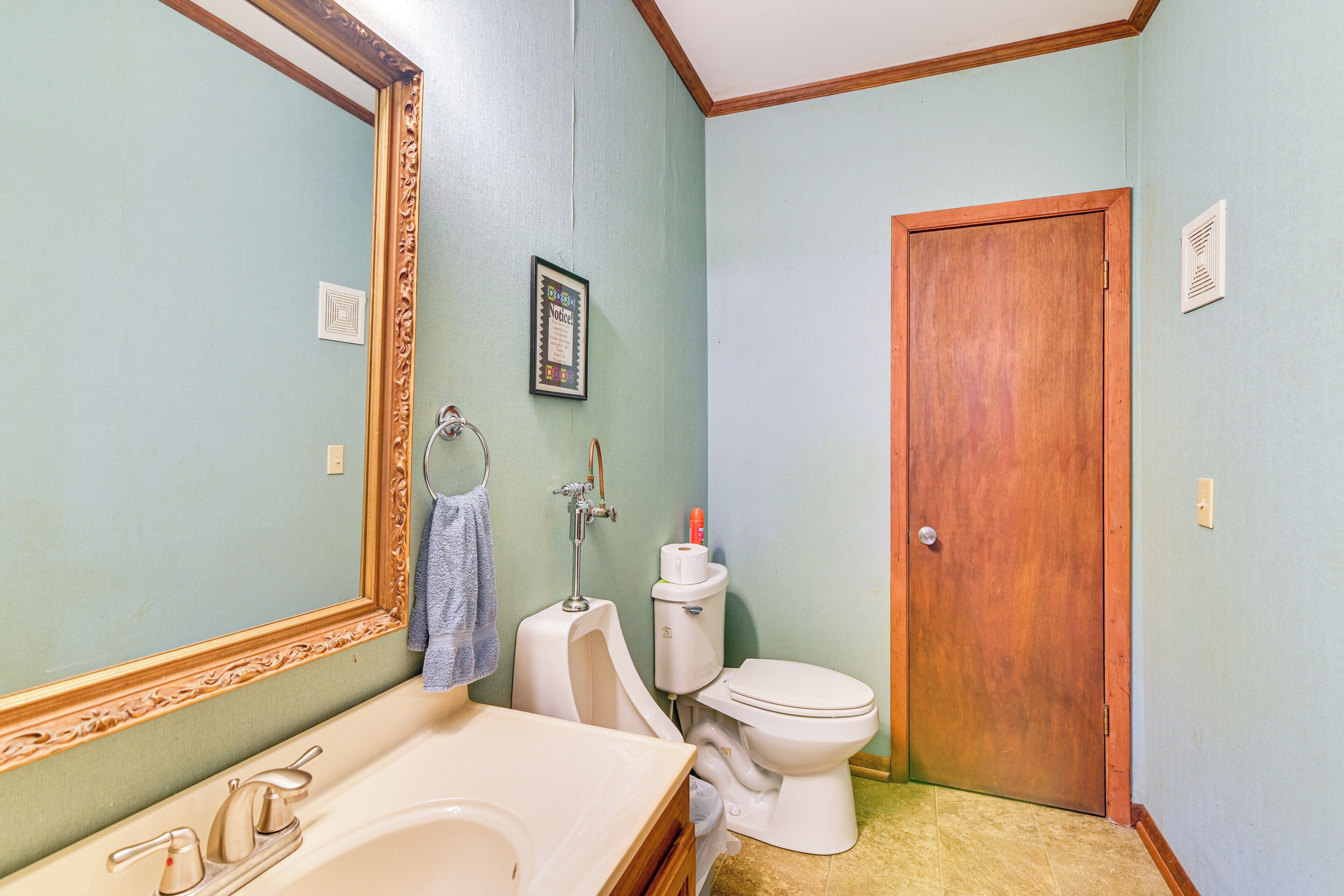 A bathroom with a sink, mirror, toilet, and wooden door.
