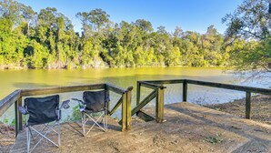 A wooden deck with two black folding chairs overlooking a lake surrounded by trees. - Riverfront Fishing: Home in Columbus w/ Grill (Columbus)