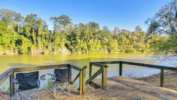 A wooden deck with two black folding chairs overlooking a lake surrounded by trees.