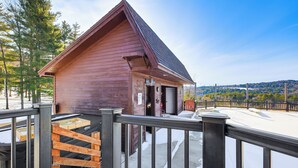 Una cabaña de madera con techo inclinado, una terraza de madera y vista a un paisaje nevado.