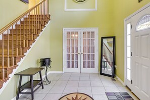 Una escalera con barandillas de madera, una puerta blanca con paneles de vidrio y una pequeña mesa con una silla.