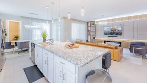 Une cuisine moderne dotée d’un îlot central, d’appareils électroménagers intégrés et de luminaires suspendus.