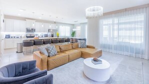 Un salon moderne avec un canapé d’angle, une table basse ronde et un coin repas équipé de tabourets de bar.