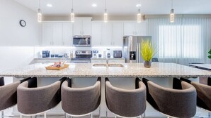 Une cuisine moderne avec des meubles blancs, un plan de travail en granit et un îlot central doté de sièges de bar.