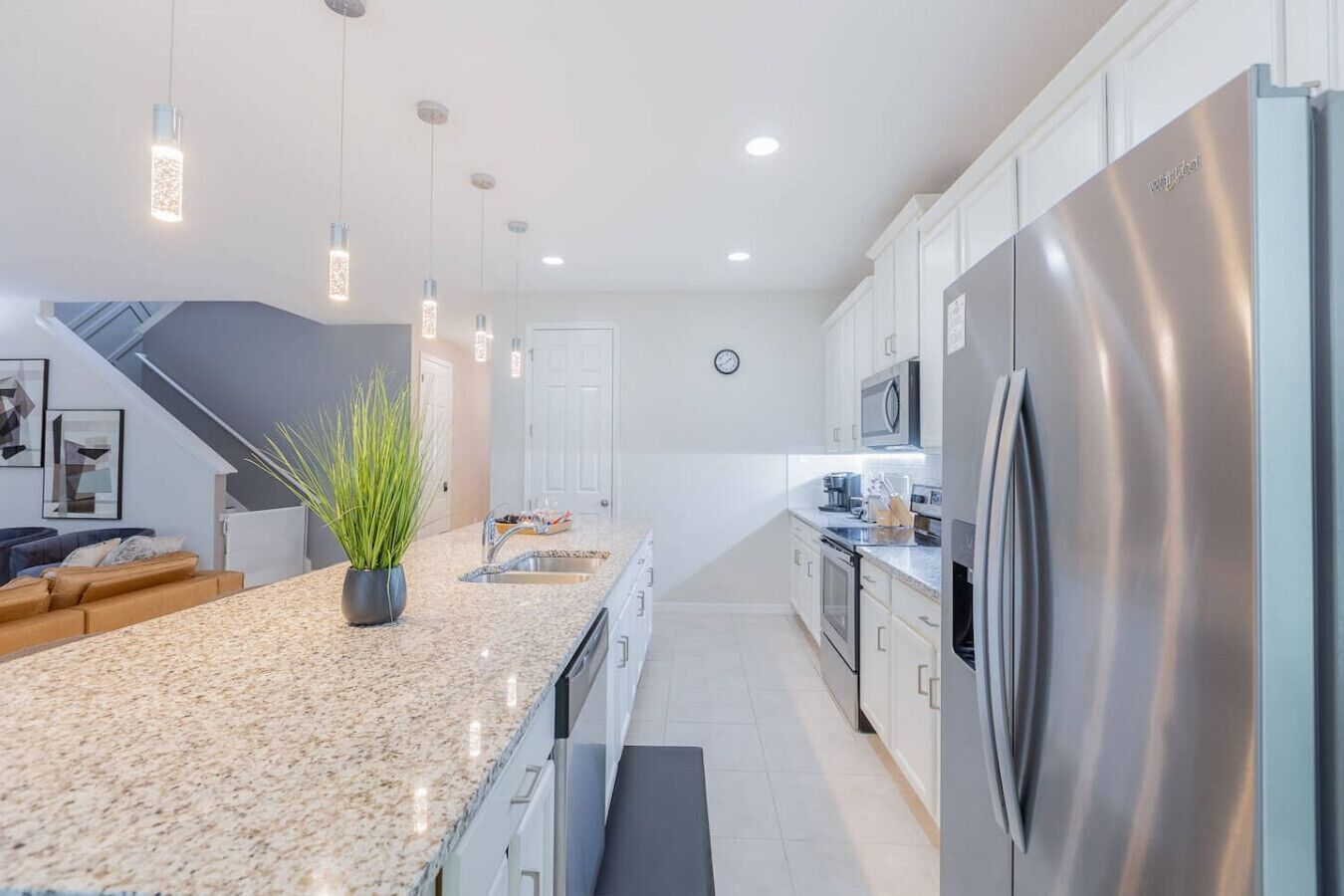 A modern kitchen with granite countertops, stainless steel appliances, pendant lighting, and a view to the living area.