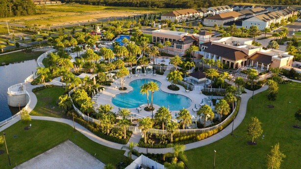 Vue aérienne d’un complexe hôtelier doté d’une piscine centrale, entouré de palmiers et de villas destinées aux clients.