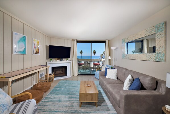 A living room with a TV, sofa, coffee table, and a view of the ocean through large windows.