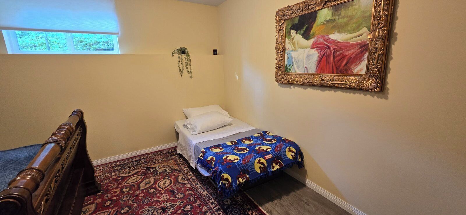 A bedroom with a bed, a window, a painting, and a patterned rug.