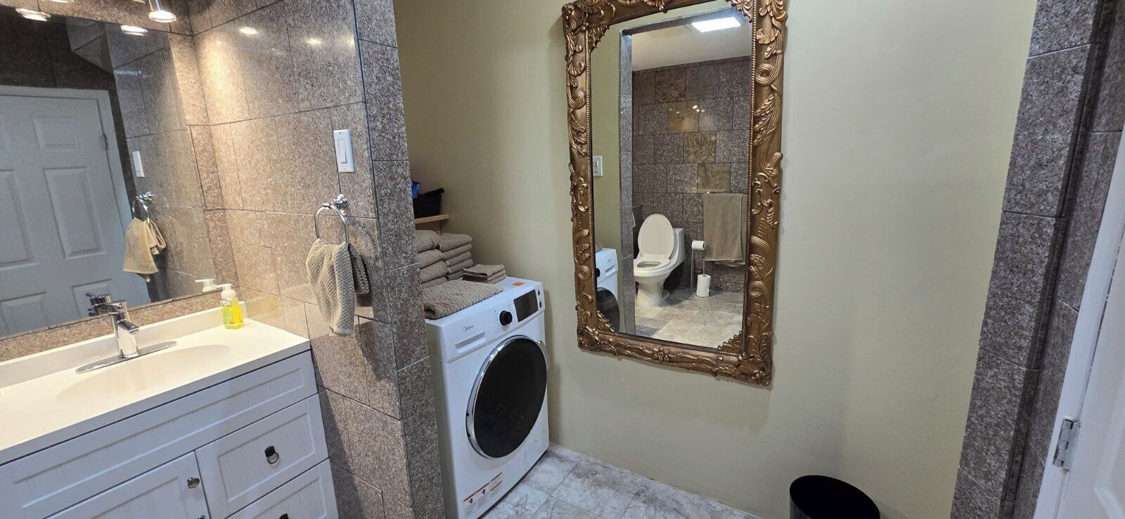 Une salle de bain équipée d’un lave-linge, d’un lavabo, d’un miroir et de serviettes.