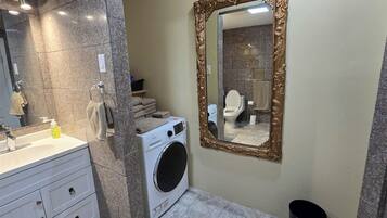 Une salle de bain équipée d’un lave-linge, d’un lavabo, d’un miroir et de serviettes.