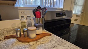 Una encimera de cocina con una tabla de cortar de madera que sostiene sal, pimienta y un tarro de leche. Un electrodoméstico de acero inoxidable se observa al fondo.