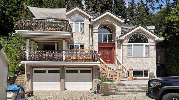 Una casa de dos pisos con un garaje, un balcón con barandillas de metal ornamentadas y una escalera que conduce al segundo piso.