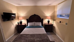Un dormitorio con una cama, dos mesitas de noche, lámparas, un televisor y una ventana con persianas.