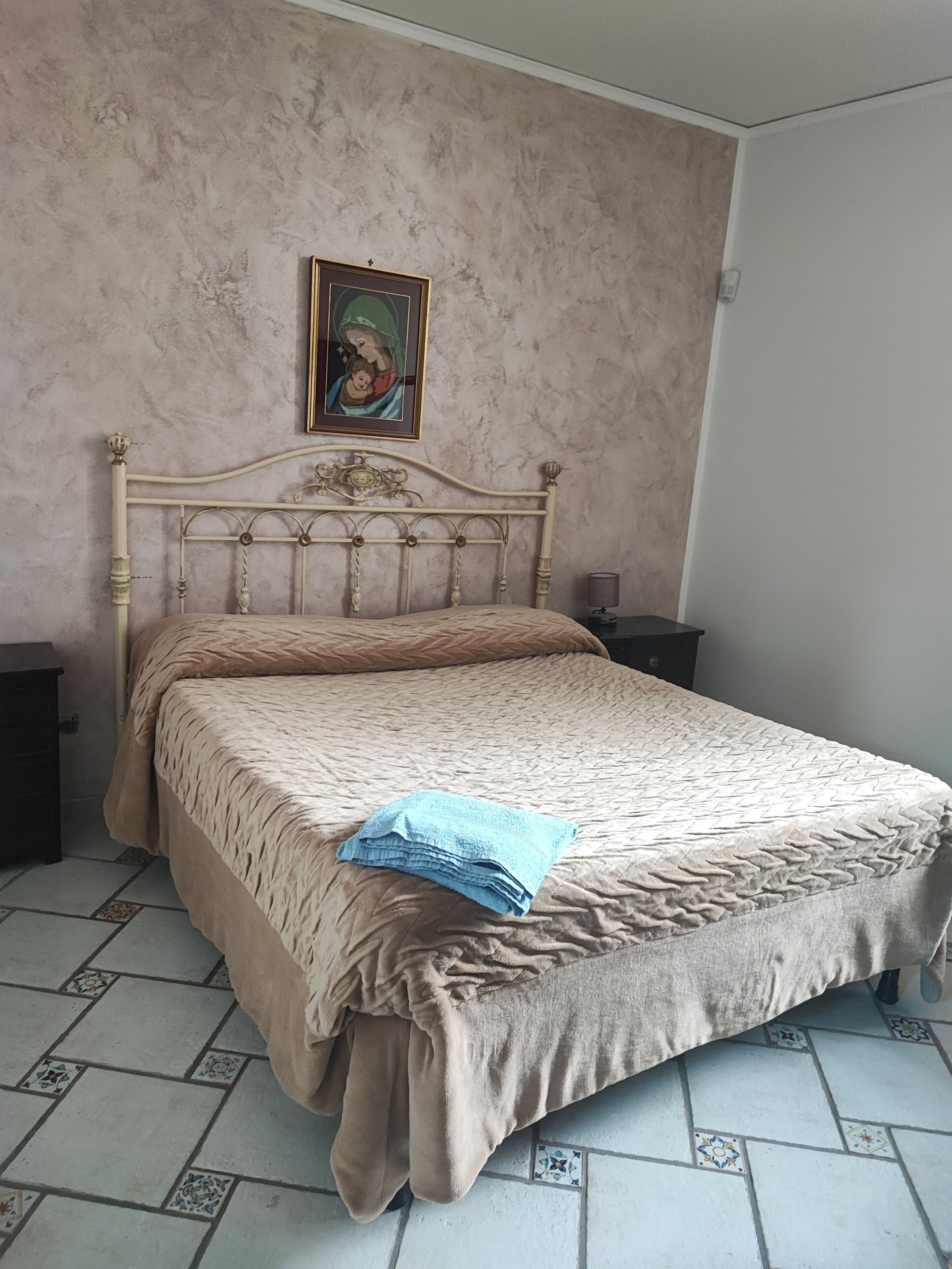 Une chambre à coucher avec un lit, une table de chevet, un tableau encadré au mur et un sol carrelé.