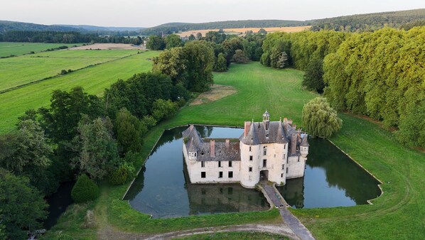 Un castillo rodeado de exuberante vegetación y campos, con un foso.