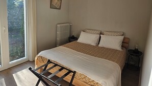 A bedroom with a bed, a radiator, a small table, and a window with curtains.