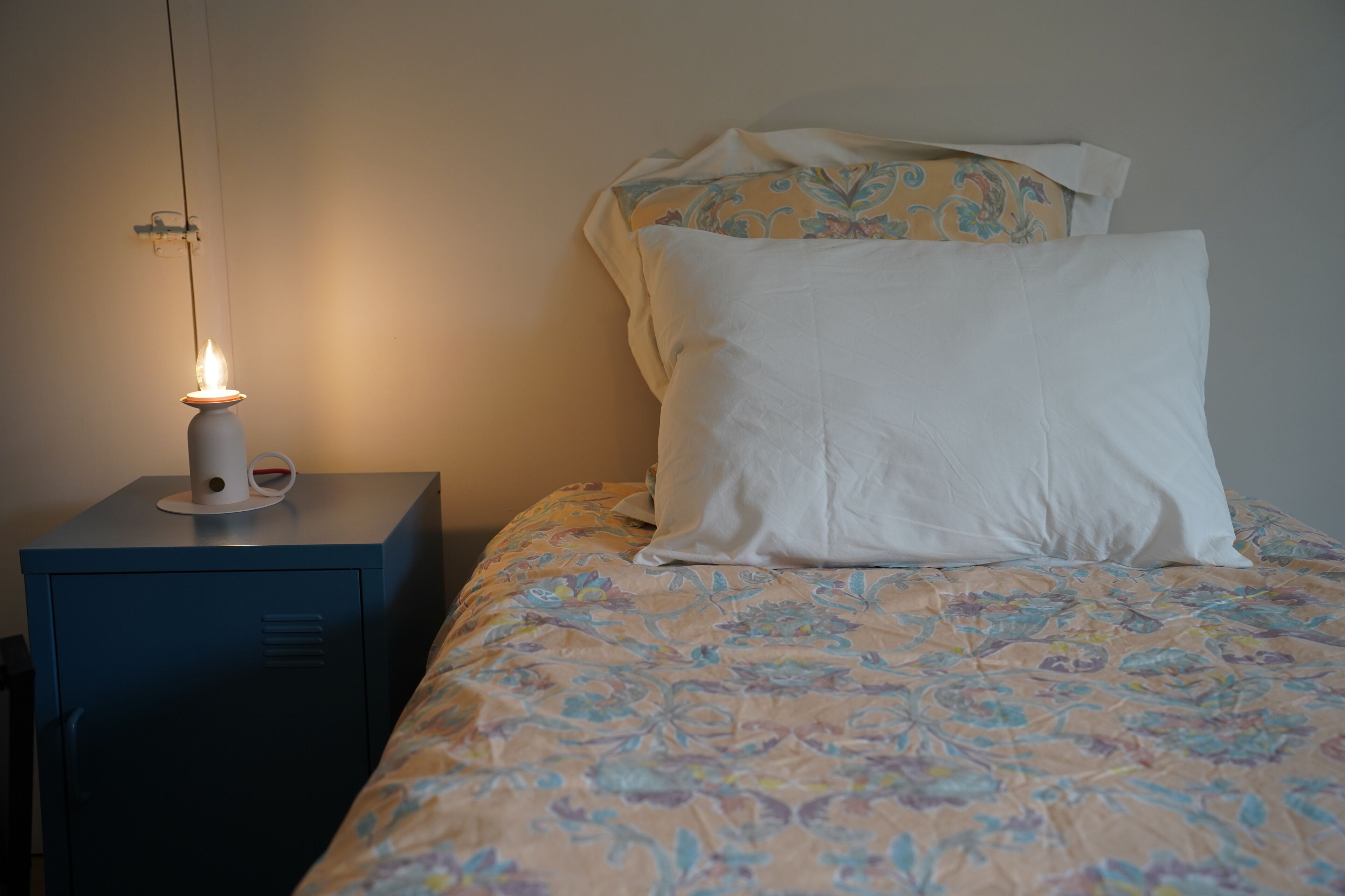 Una cama con un edredón estampado con motivos florales, una lámpara de noche y una mesita de noche con lámpara.