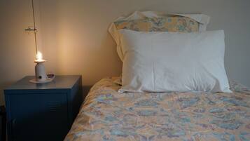 Una cama con un edredón estampado con motivos florales, una lámpara de noche y una mesita de noche con lámpara.