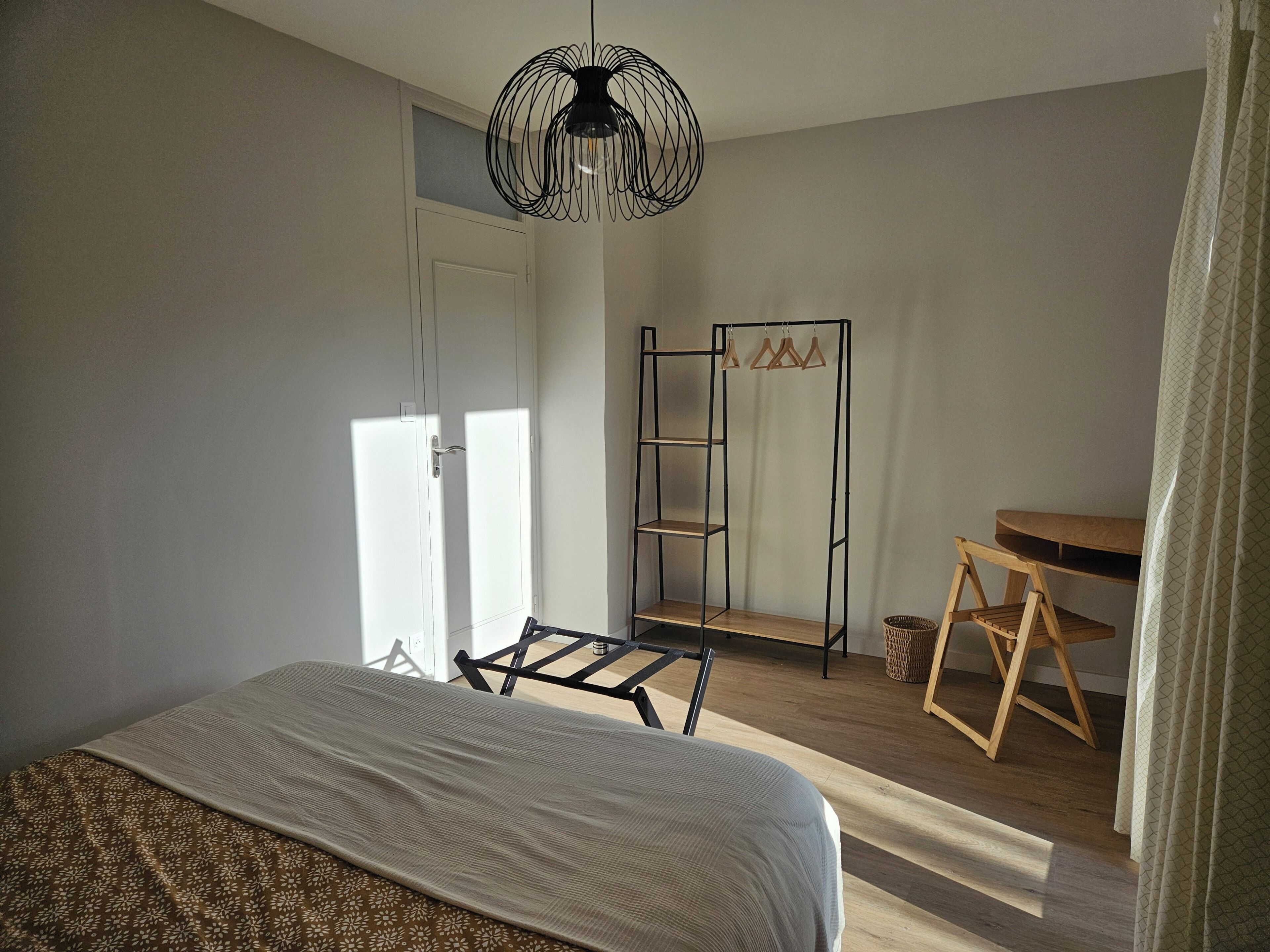 Quarto com cama, luminária pendente, uma cadeira de madeira e um aparador.